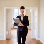 Smiling beautiful saleswoman holding file at empty new apartment. Portrait of female real estate agent. She is wearing blazer.